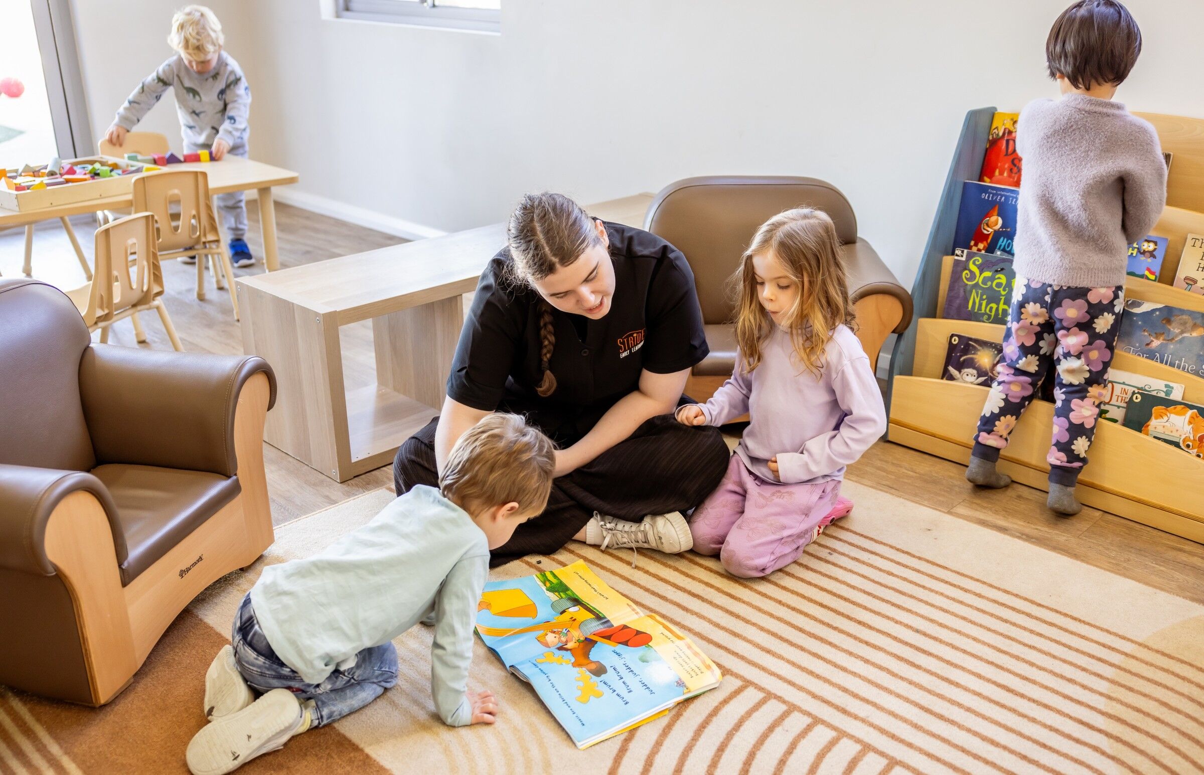 Looking for Childcare Over the Christmas & New Year Break? We’re Here to Support Your Family Early learning educator reading a book with young children in a childcare room.